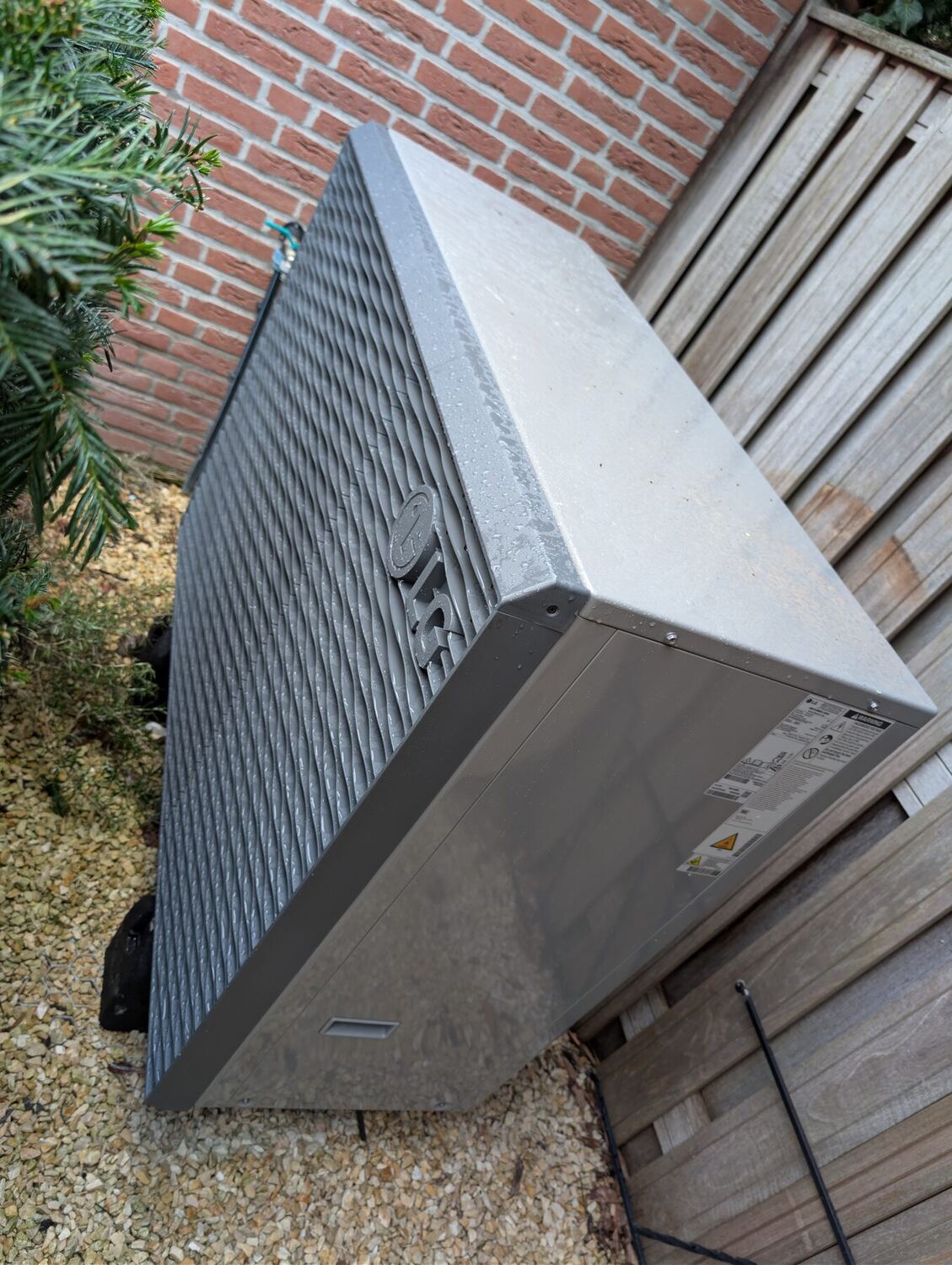 Buitenunit van een warmtepomp op trillingsdempers, geplaatst langs de gevel