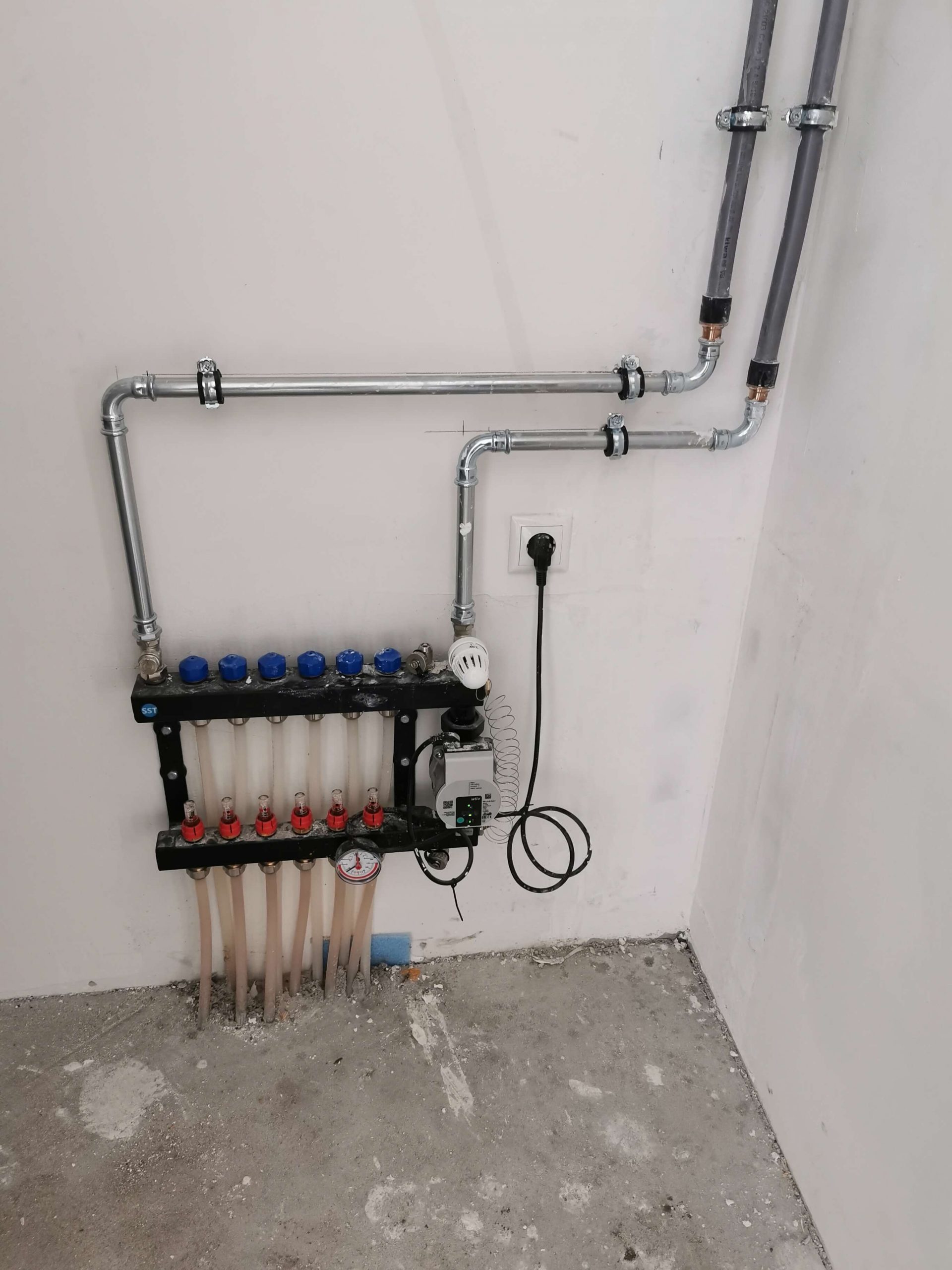 Verdeler voor vloerverwarming met circulatiepomp, aangesloten op de wand in een woning
